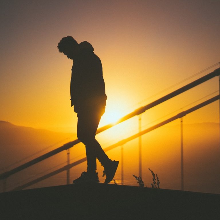 A silhouette of a young male walking on the staircase behind stair rails with beautiful sunset view in the background
